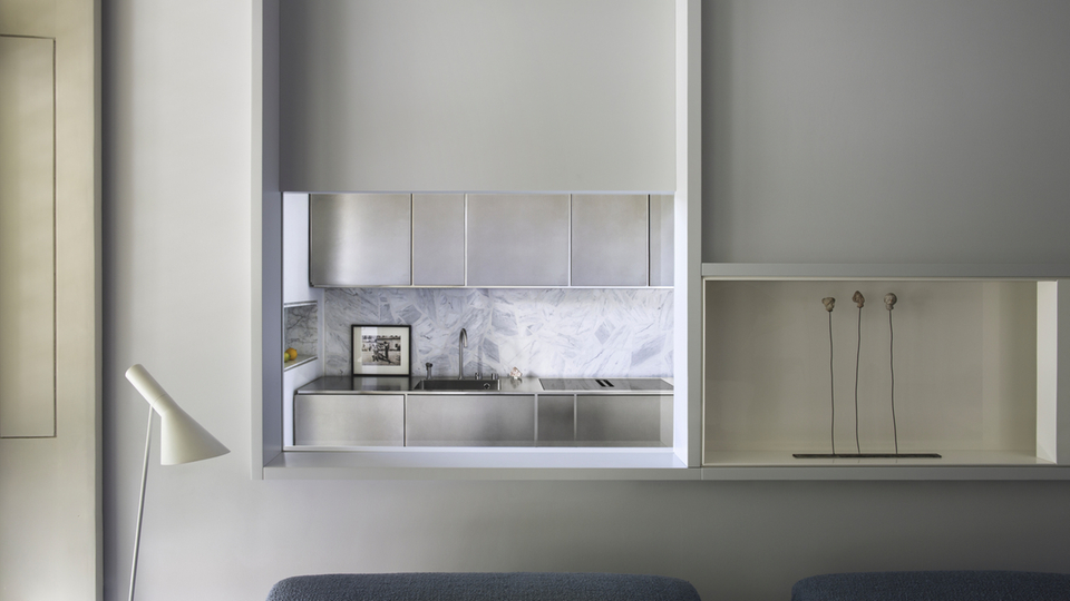 Cucina minimalista con frontali in acciaio inossidabile, lavello e alzatina in marmo chiaro in un ambiente moderno