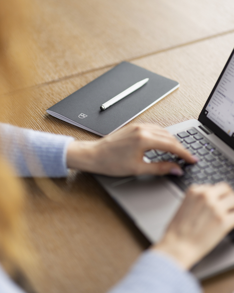 Nahaufnahme eines Notebooks und eines Laptops auf einem Holztisch mit tippender Person